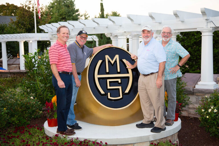 MHS Alum standing around a large MHS class ring.